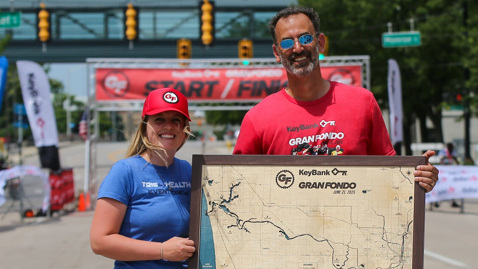 Two people holding a framed map at a race start/finish line.